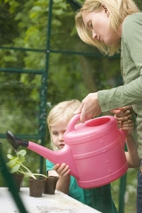 Young blonde girl helping woman watering seedling pots in the greenhouse with pink watering can