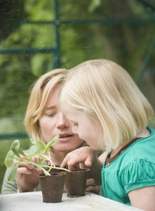 Young blonde girl helping woman tending seedlings in the greenhouse