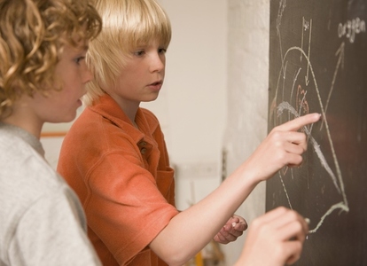Two young boys writing on a blackboard