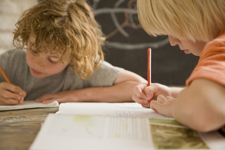 Two young boys writing and sitting at desk in the classroom