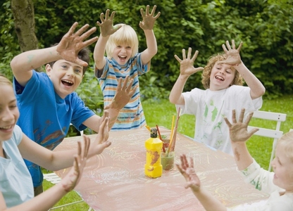 Children smiling and laughing with their arms up and hands covered in paint