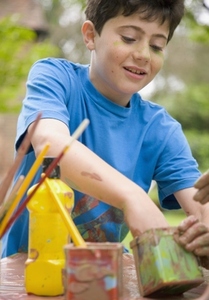 Young boy smiling with one hand in a watercolor paint container