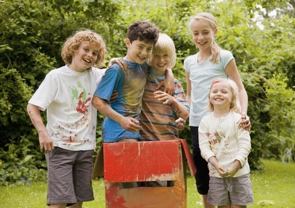 Children covered in watercolor paint in a garden two of them standing in a cardboard box