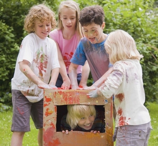 Children covered in watercolor paint playing in a garden one of them is in a cardboard box