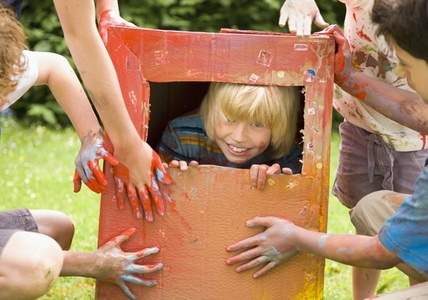 Young blonde boy trapped  in a cardboard box playing with friends