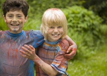 Two young boys covered in watercolor paint laughing in a garden