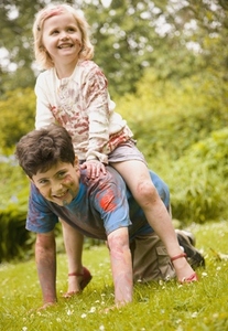 Young girl riding piggyback on young boy both dirty with watercolor paint