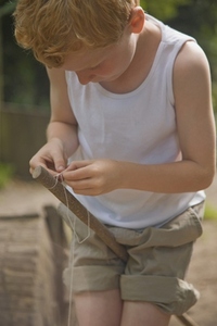 Young boy holding wooden stick between legs tying a knot with a string