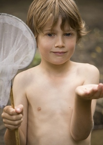 Young boy holding a fishing net with a tadpole on his hand
