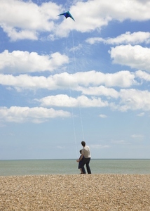 Back view of father and son standing on a beach flying a kite