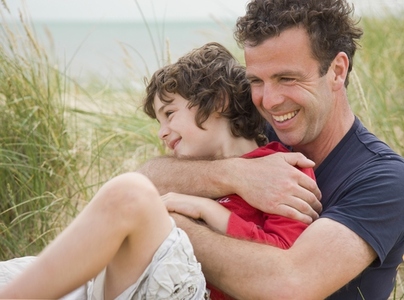 Father and son sitting on a beach smiling and embracing