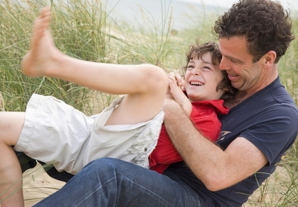 Father and son sitting on a beach smiling and fighting