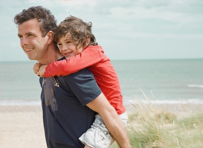 Young boy riding piggyback on his father shoulder on a beach