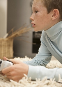 Profile of a young boy lying on a rug and holding a video game control