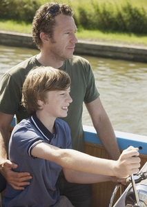 Man and smiling teenaged boy steering a boat