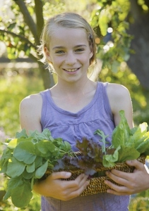 Smiling young girl standing in a garden holding a basket of leafy vegetables