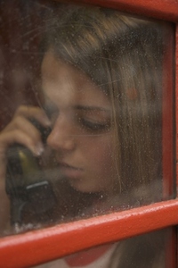 Teenaged girl talking on the telephone inside a London phone booth