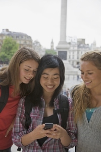 Three smiling teenaged girls using a cell phone in London Trafalgar Square