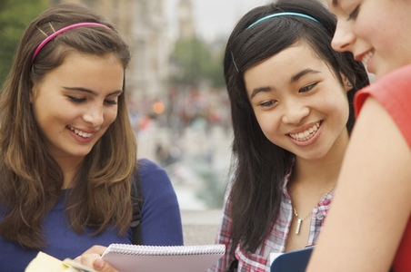 Three smiling teenaged girls reading writing and holding note pads