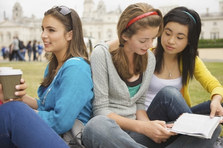 Teenaged girls sitting in front of London Horse Guards Parade drinking coffee and reading a book