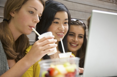 Teenaged girls using laptop computer drinking milk shake