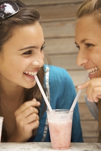 Two smiling teenaged girls drinking milk shake with a straw from the same glass