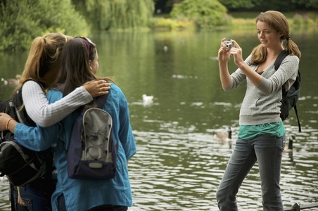Teenaged girl taking photograph of two women by a lake