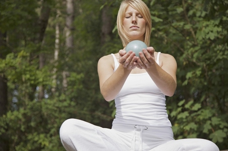 Young woman in meditation sitting cross legged by a forest holding a sphere in her hands