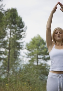 Young woman doing yoga standing in a forest in the raised hands pose