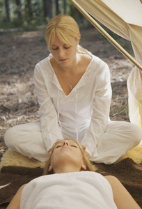 Female massage therapist sitting behind a woman massaging her scalp under a tent