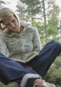 Young woman sitting cross legged in a forest reading a book