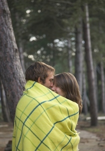 Young couple standing in a forest wrapped in a blanket looking at each other