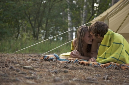 Young couple lying in front of a tent entrance looking at each other
