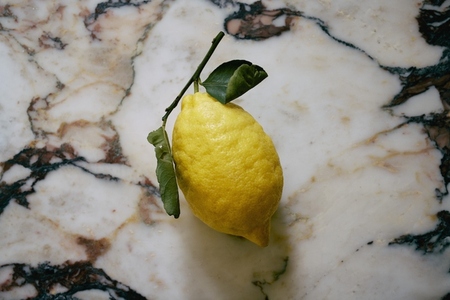 Still life vibrant yellow lemon on stem against granite countertop