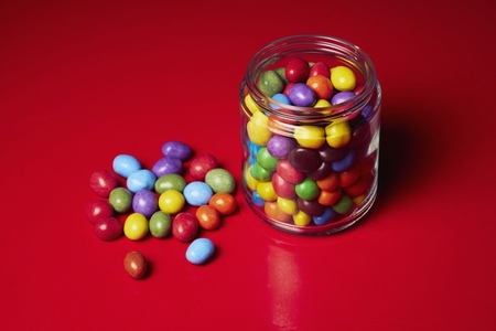 Still life multicolored candy in glass jar on red background