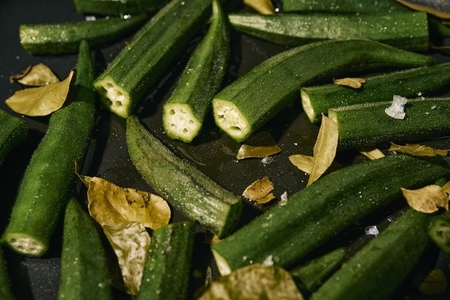 Close up vibrant green okra and leaves cooking in pan with oil and salt