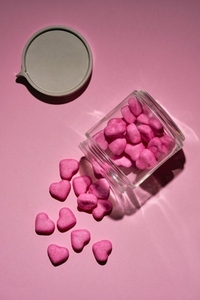 Pink candy hearts spilling from glass jar on pink background
