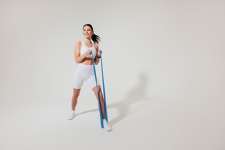 Positive woman in white fitness attire warming up her arms with a resistance band