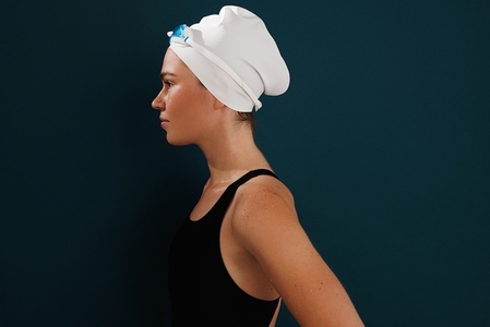 Side view of a woman swimmer standing at blue wall  wearing swimming cap and glasses