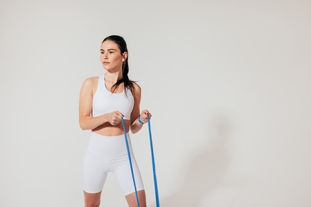 Young fit woman in white sportswear exercising with resistance band