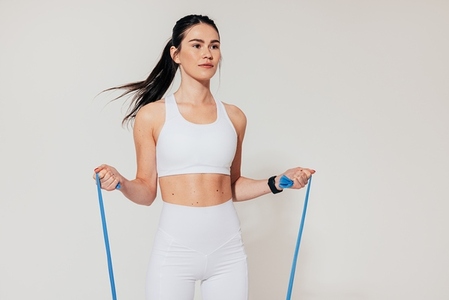 Fit woman in white sports clothes exercising with resistance band in studio
