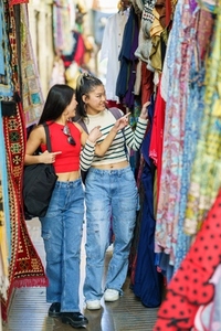 Two Asian girls tourists shopping clothes in street bazaar