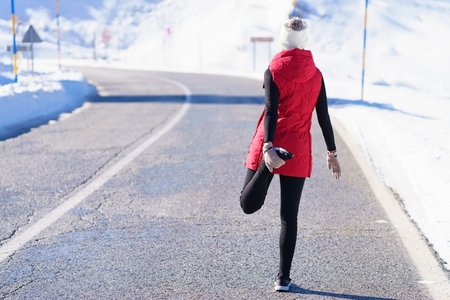 Unrecognizable sportswoman warming up on winter road
