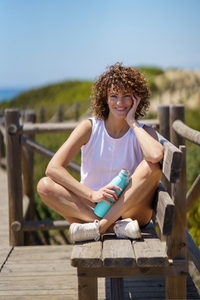 Smiling sportswoman with bottle of water sitting on wooden bench
