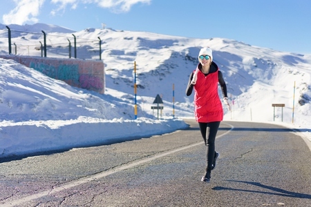 Young woman running on road near snow and warming up