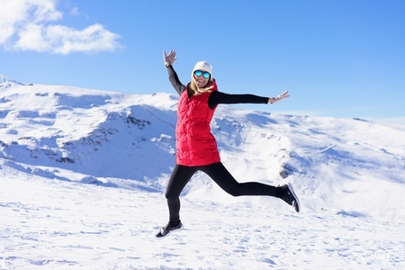 Carefree young woman jumping and enjoying vacation on snowy slope