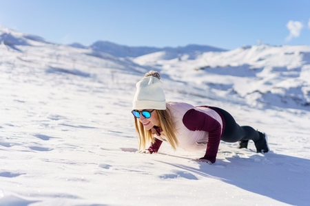 Woman in goggles in yoga pose on snowy plain