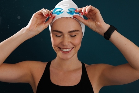 Close up portrait of a smiling woman swimmer wearing a swimming cap and goggles