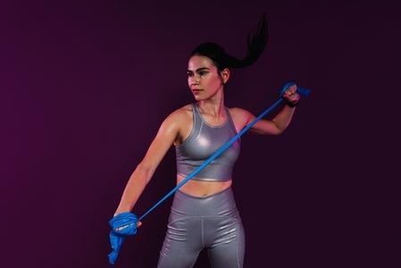 Slim woman wearing silver fitness attire exercising with resistance band