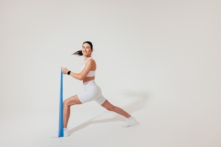 Young slim female in white fitness attire practicing with a resistance band in a studio